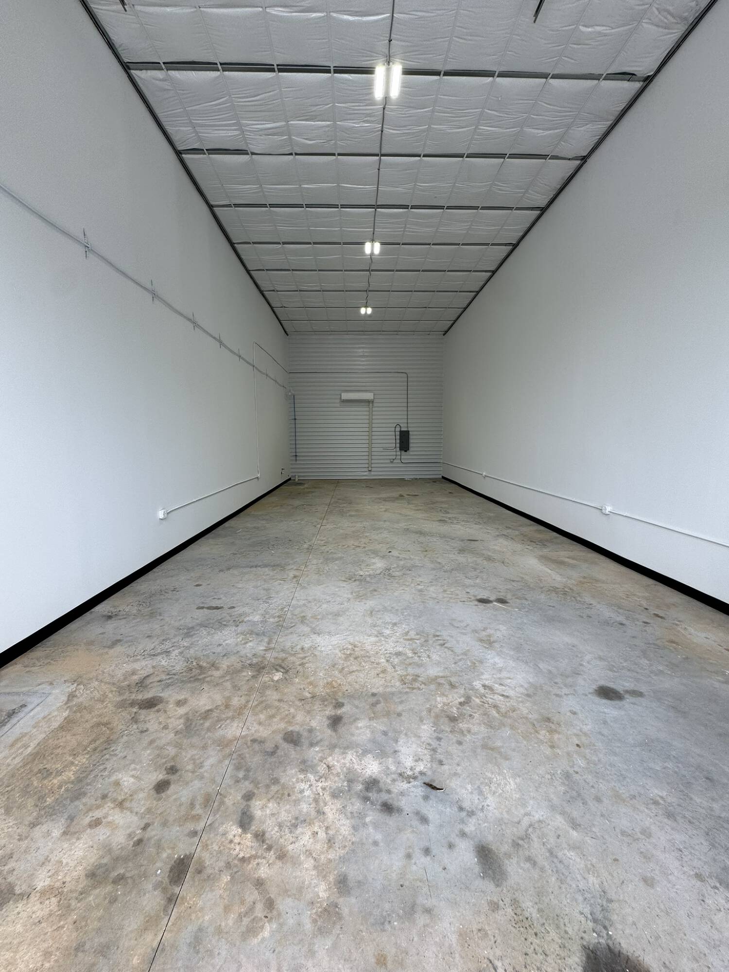 Empty flex unit interior with white walls, insulated ceiling, and a rear roll-up door