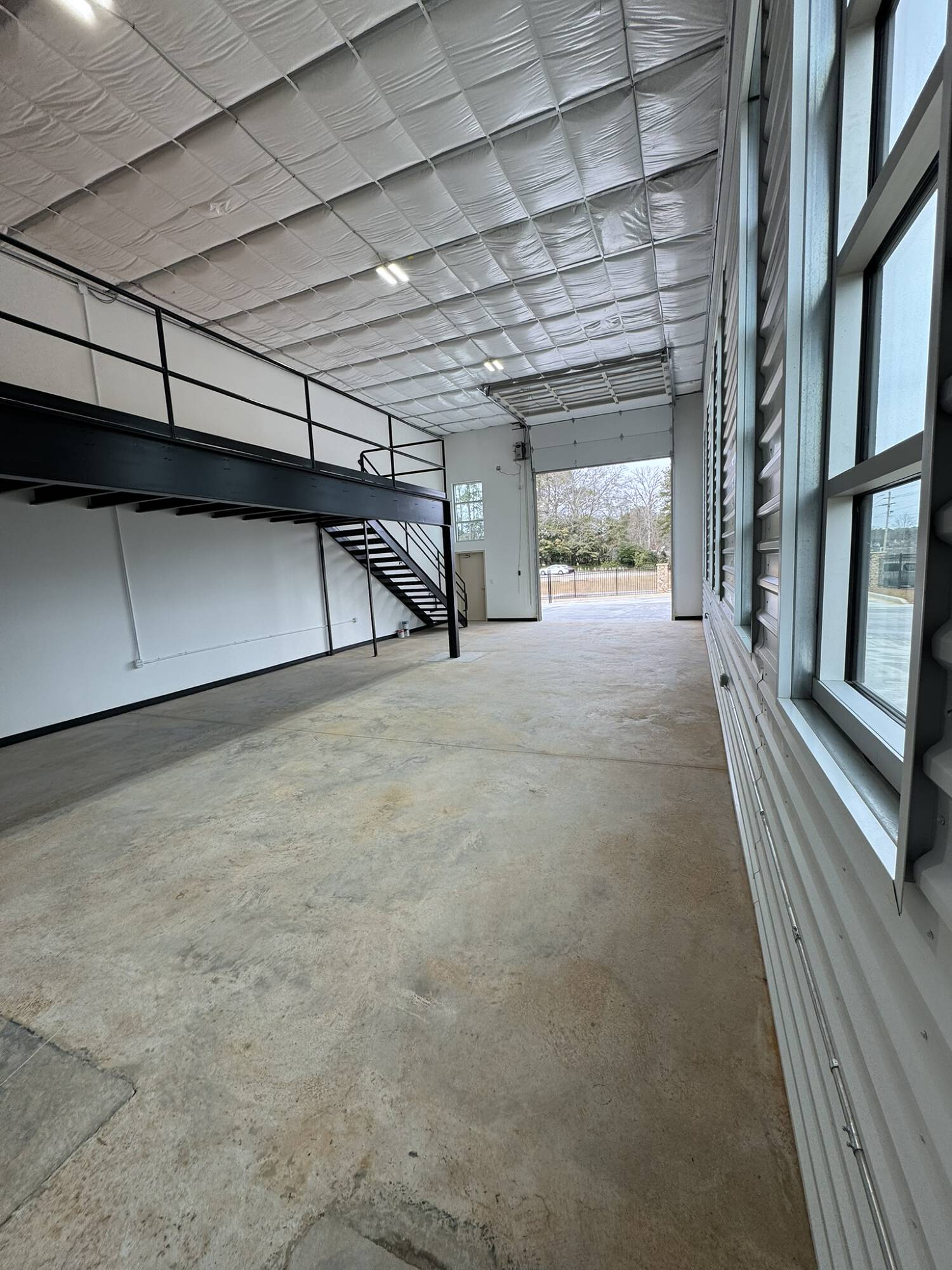 Flex unit with an open roll-up bay door, mezzanine loft, and tall windows along the wall
